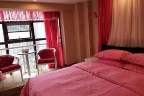 A hotel room with a large bed, two chairs, a small table, and a window with curtains. - Mingdu International Hotel (Bazhong)