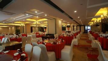 A banquet hall with round tables, white chairs, and red tablecloths.