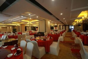 Une salle de banquet avec des tables rondes, des chaises blanches et des nappes rouges.