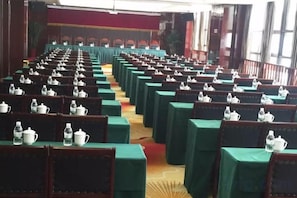 Une salle de conférence avec des rangées de tables et de chaises, chacune étant équipée d’une théière et d’une bouteille d’eau.