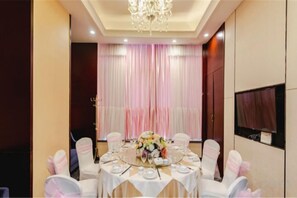 Een balzaal met ronde tafels, witte tafelkleden en roze stoelen.