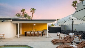 A pool area with lounge chairs, a dining setup, and a stone wall.