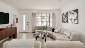 A modern living room with a sectional sofa, a coffee table, and a flat-screen TV mounted on the wall.