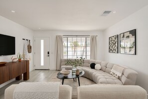 A modern living room with a sectional sofa, a coffee table, and a flat-screen TV mounted on the wall.