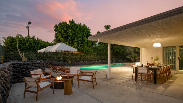 An outdoor patio area with a pool, lounge chairs, a table, and a fire pit.