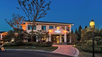 A hotel with a well-lit entrance, a curved driveway, and a landscaped garden.