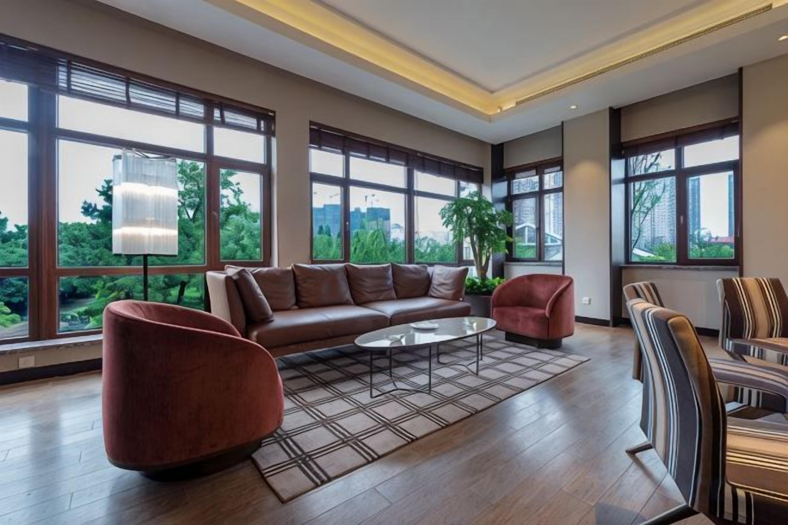 A spacious living room with a sectional sofa, a coffee table, and a view of greenery through large windows.