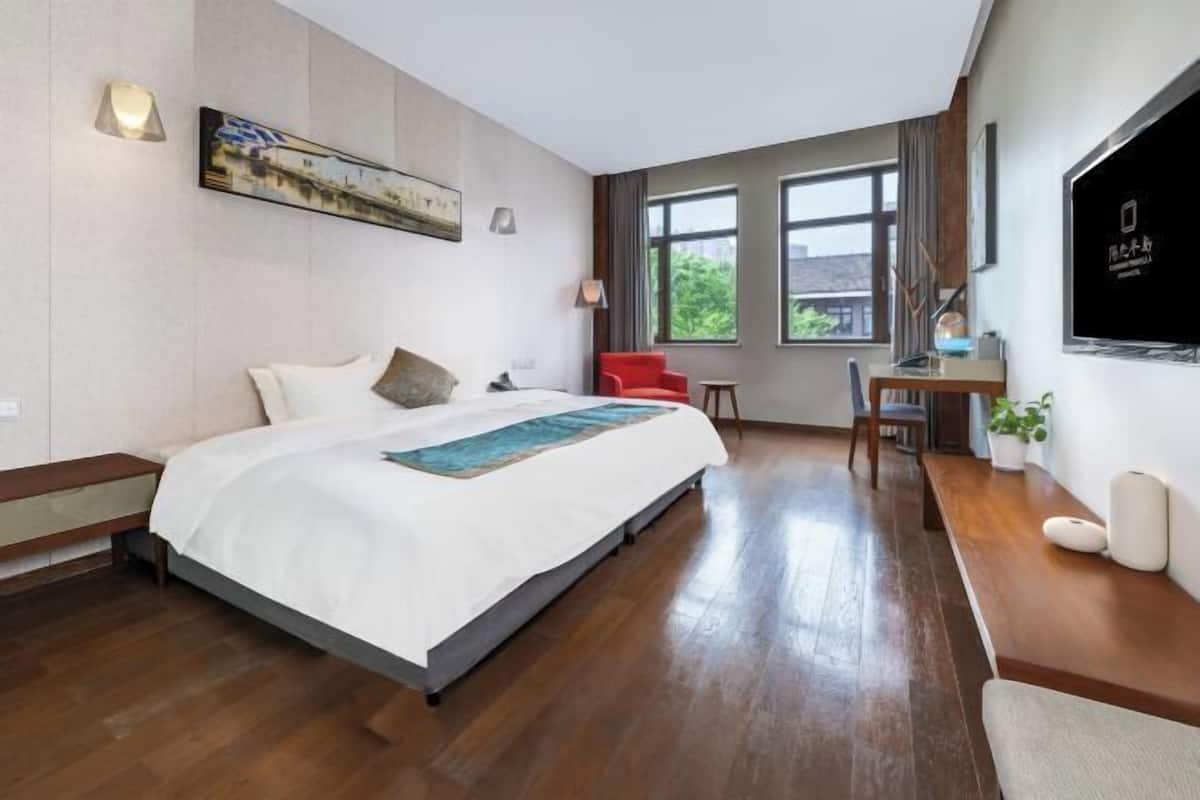 Ein Hotelzimmer mit Bett, Schreibtisch, Stuhl, Fernseher und großen Fenstern.