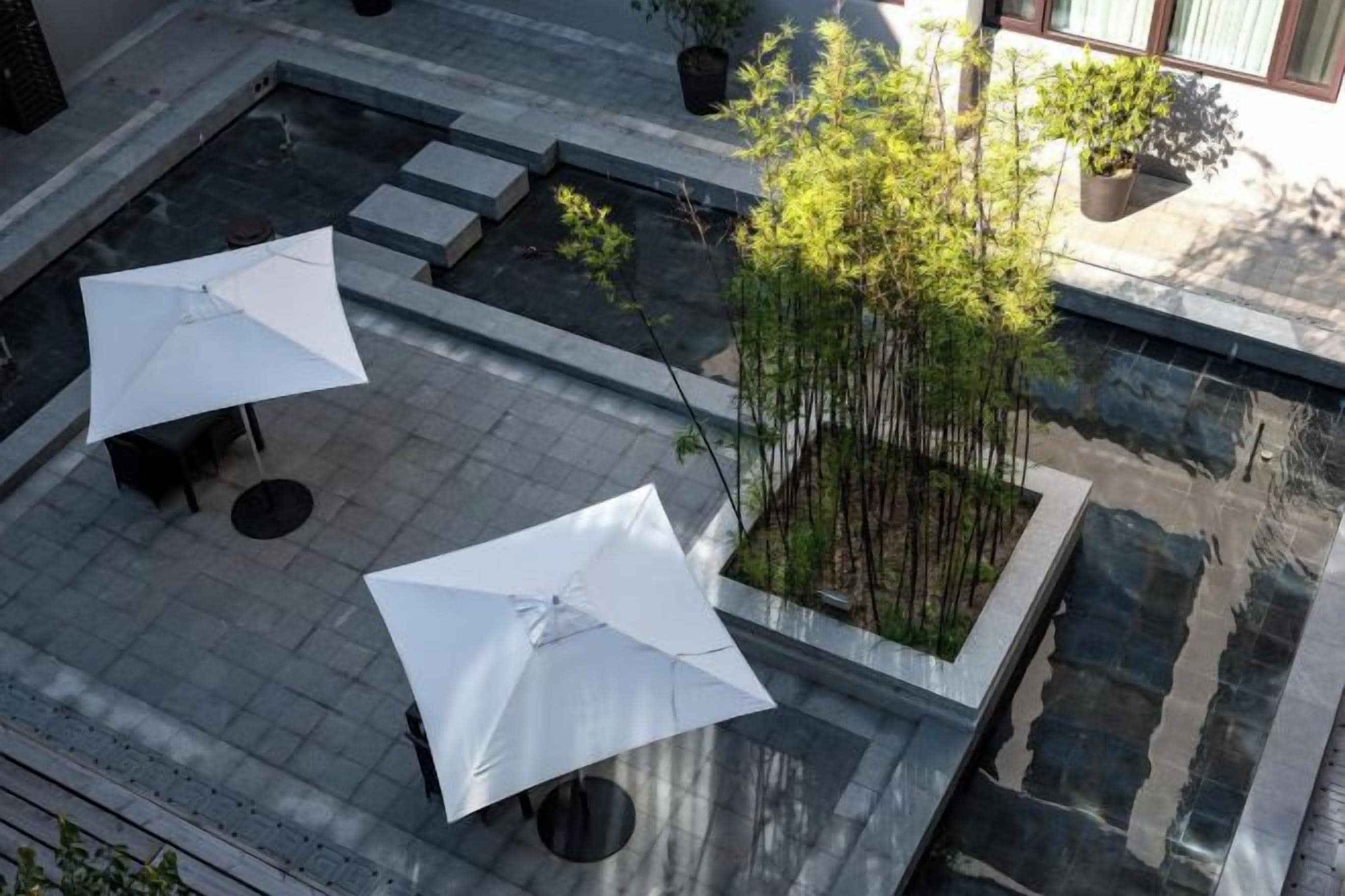 An outdoor patio area with two white umbrellas, a small seating area, and a bamboo plant.