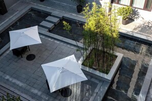 An outdoor patio area with two white umbrellas, a small seating area, and a bamboo plant. - Sunshine Peninsula Jinsha Hotel (Zhangjiagang)