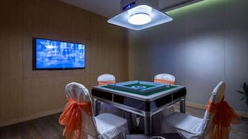 A room with a pool table, four chairs with orange sashes, a television on the wall, and a ceiling light fixture.