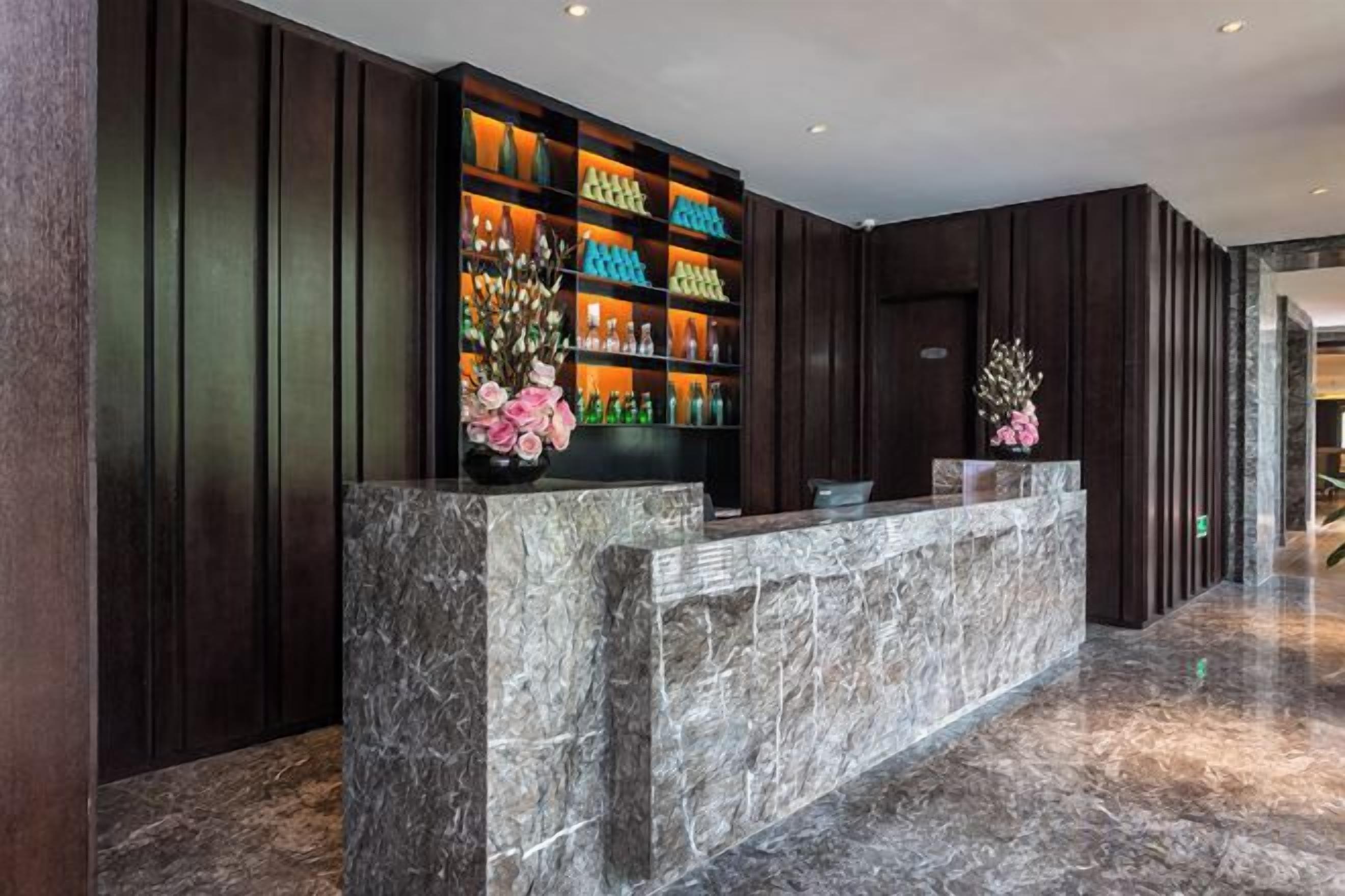 Una zona de recepción con mostrador de mármol, paneles de madera oscura y una estantería con varios objetos.