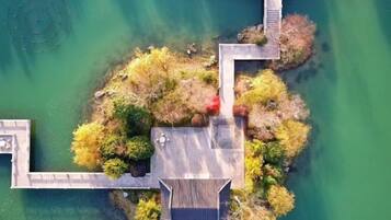 An aerial view of a lakeside property with a wooden dock, a small bridge, and a circular water feature.