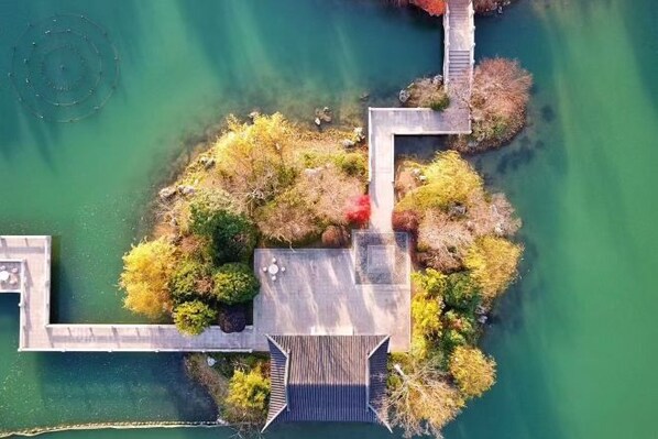 Vista aérea de una propiedad junto al lago con un muelle de madera, un pequeño puente y un estanque circular.