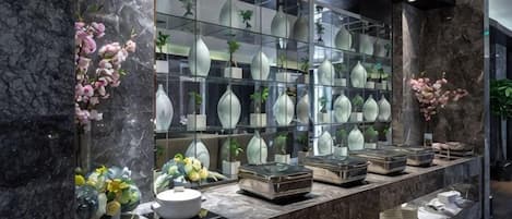 Zona de recepción con mostrador de mármol, vitrinas con jarrones y flores decorativas.