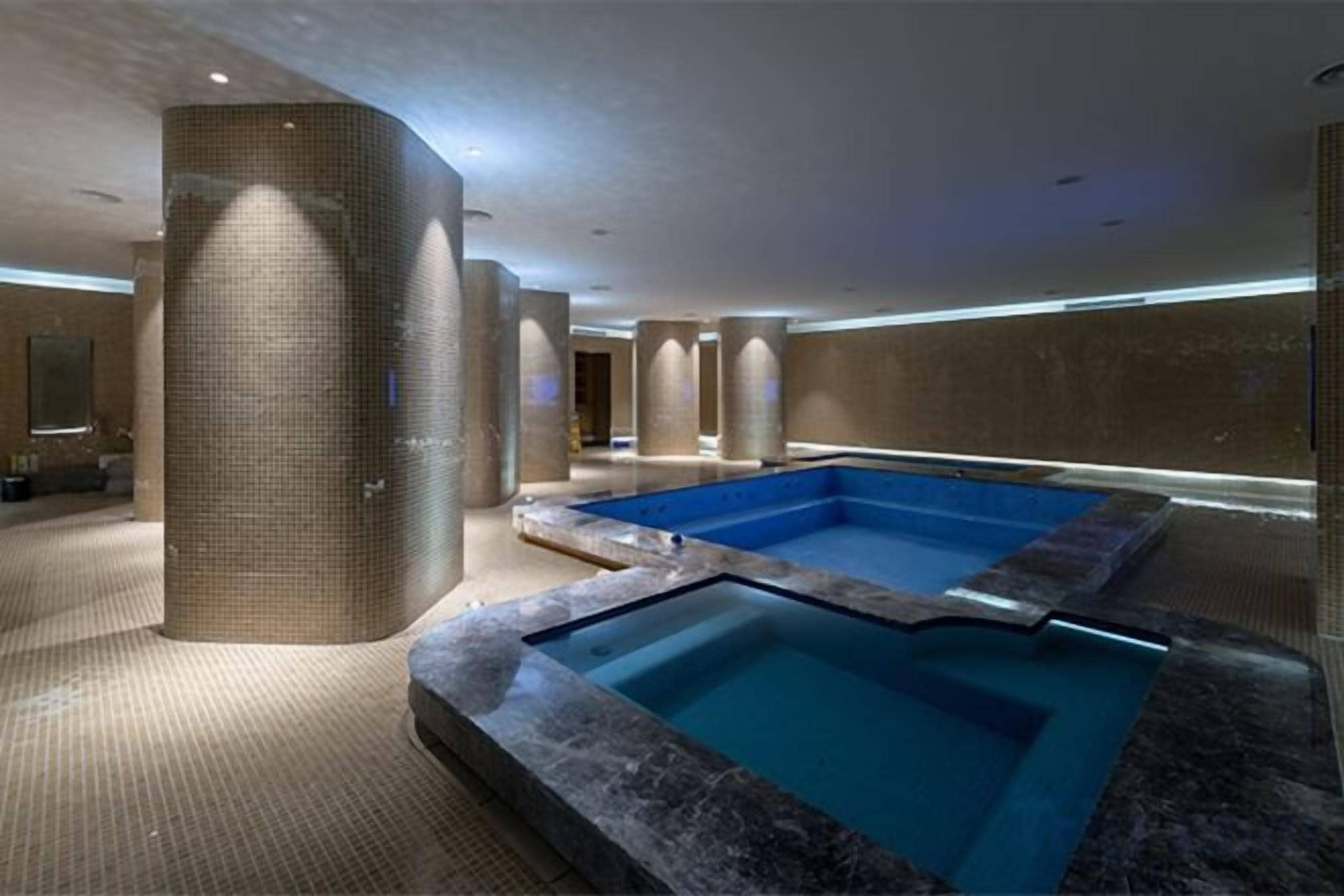 A spa area with a large hot tub, a tiled wall, and a pool.