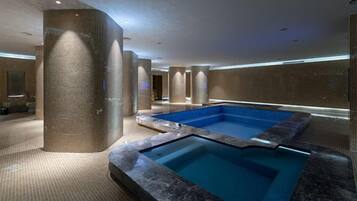 A spa area with a large hot tub, a tiled wall, and a pool.