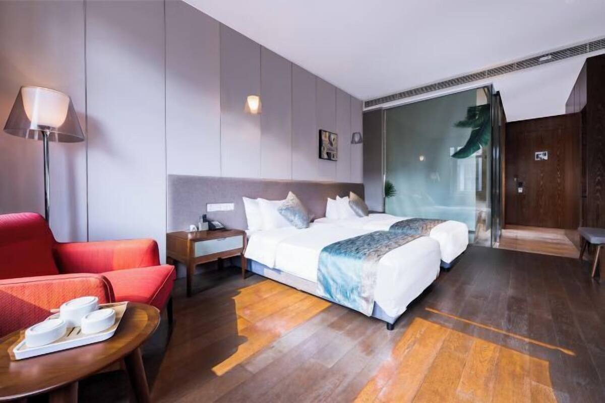 Ein Hotelzimmer mit einem Bett, einem roten Sessel, einem Nachttisch, einer Lampe und einer Glastür, die auf einen Balkon führt.
