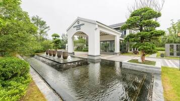 A building with a covered entrance, a water feature, and a well-maintained garden.