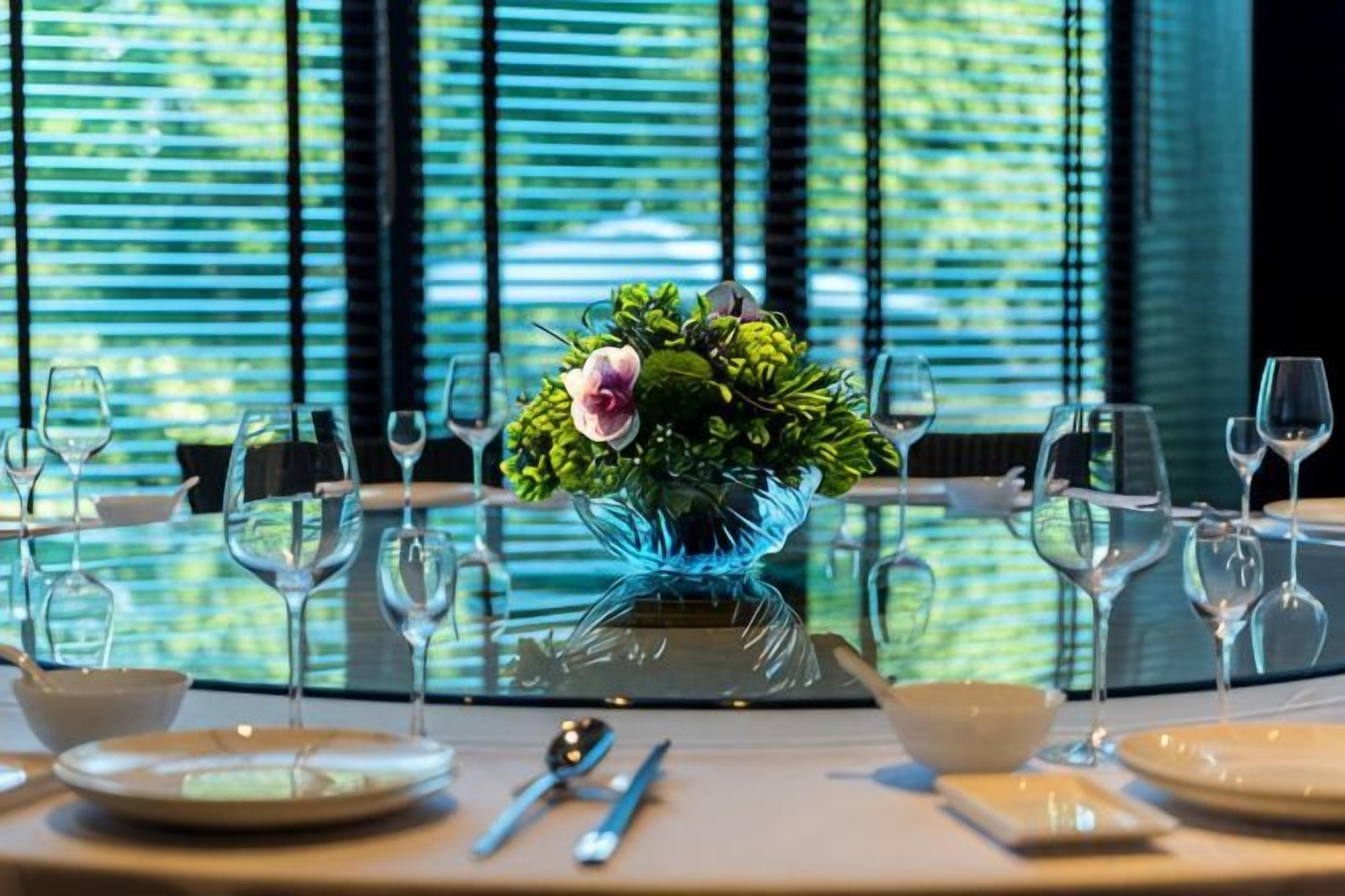 A dining table set with plates, cutlery, and wine glasses, with a decorative vase in the center.