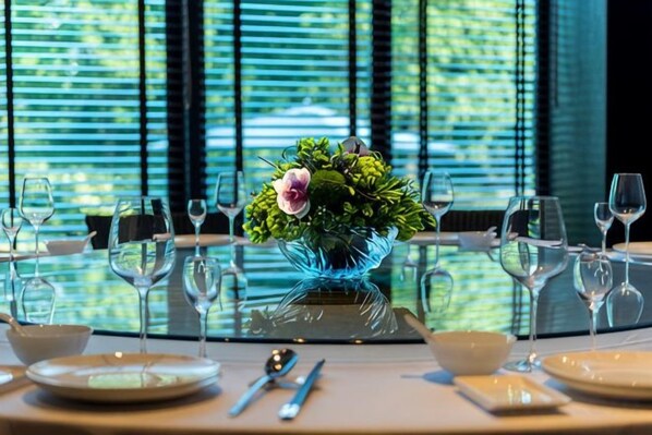 Une table à manger dressée avec des assiettes, des couverts et des verres à vin, et un vase décoratif placé au centre.
