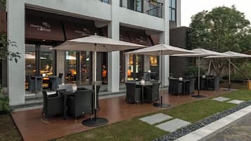 An outdoor seating area with tables and umbrellas, a paved walkway, and a building with a storefront.