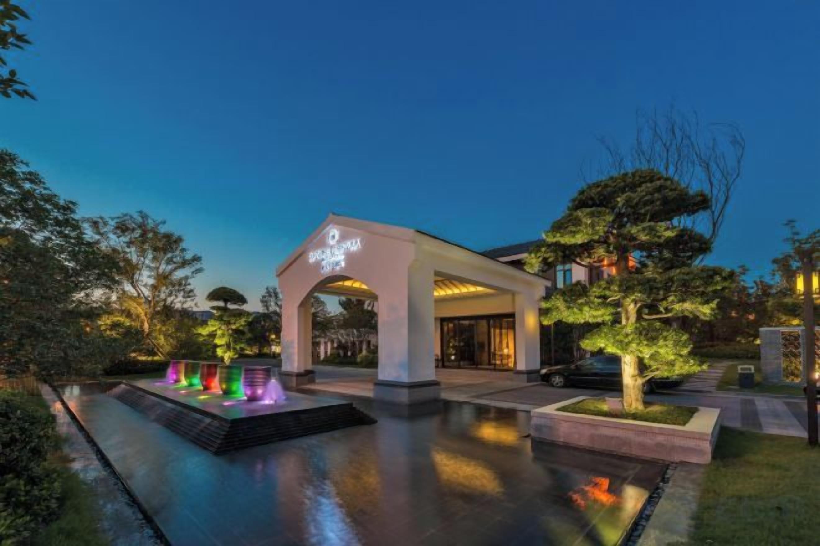 A hotel entrance with a covered walkway, a water feature, and a well-maintained garden.