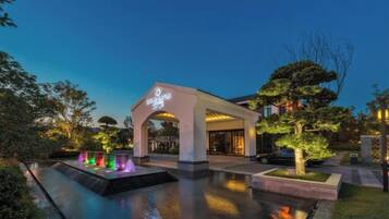 A hotel entrance with a covered walkway, a water feature, and a well-maintained garden.