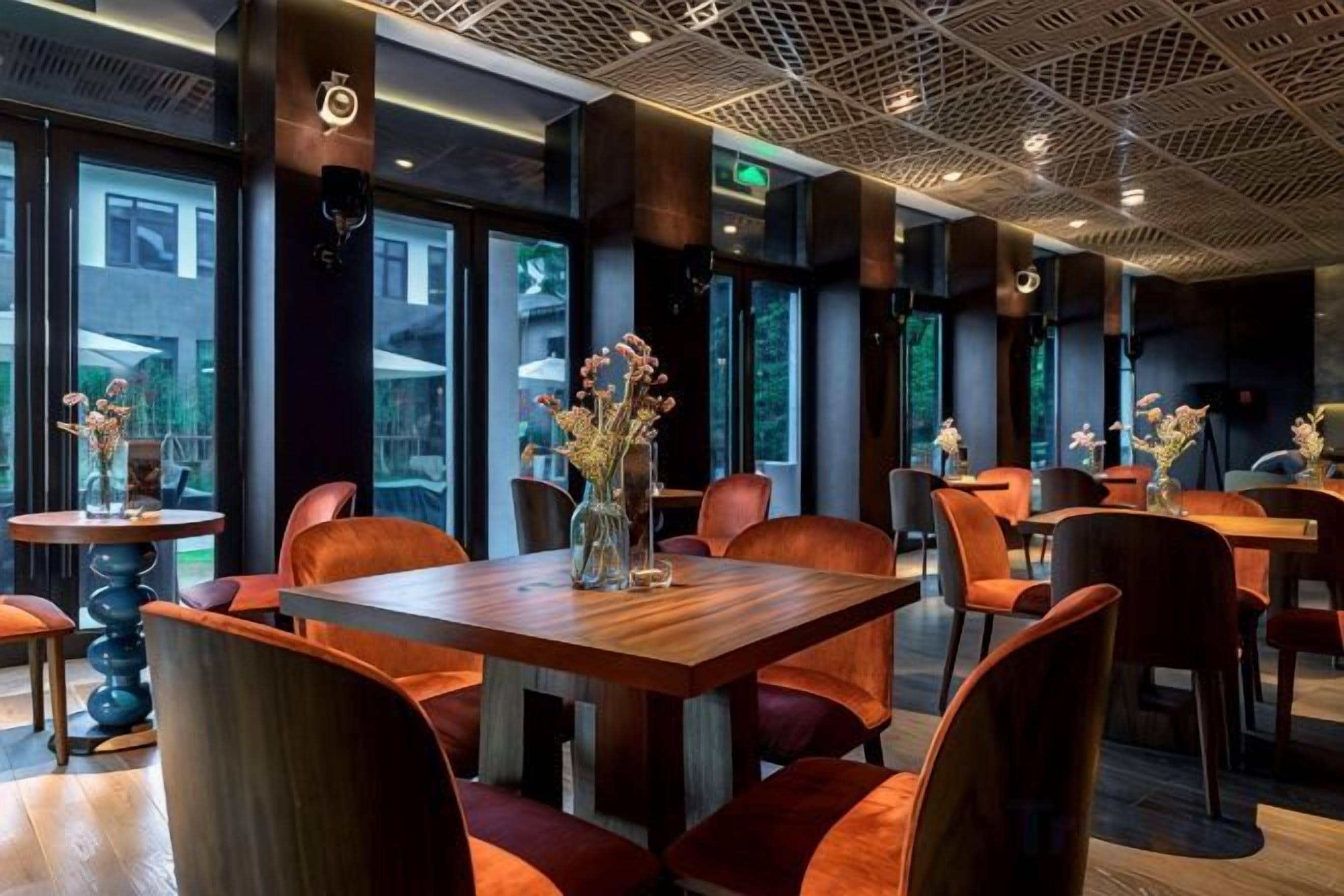 A modern restaurant interior with wooden tables and orange chairs, large windows, and decorative vases.