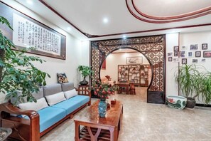 A living room with a blue sofa, a wooden coffee table, and a decorative archway leading to a dining area. - Jiaxin Hotel (Pingbian)