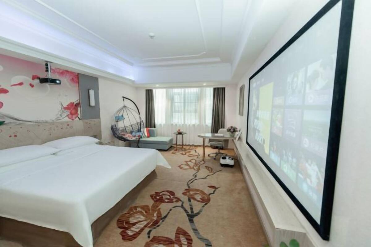 A hotel room with a bed, a desk, a chair, a TV screen, and a decorative wall.