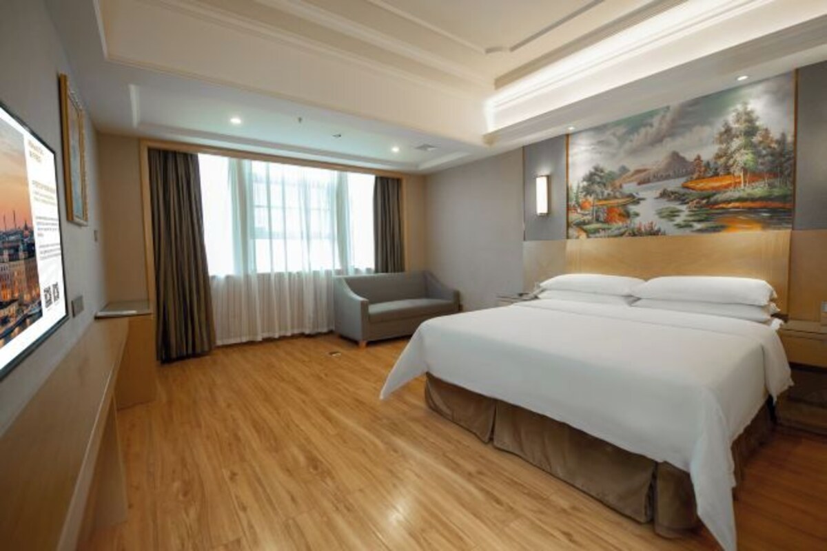 A hotel room with a large bed, a desk, a chair, and a painting on the wall.