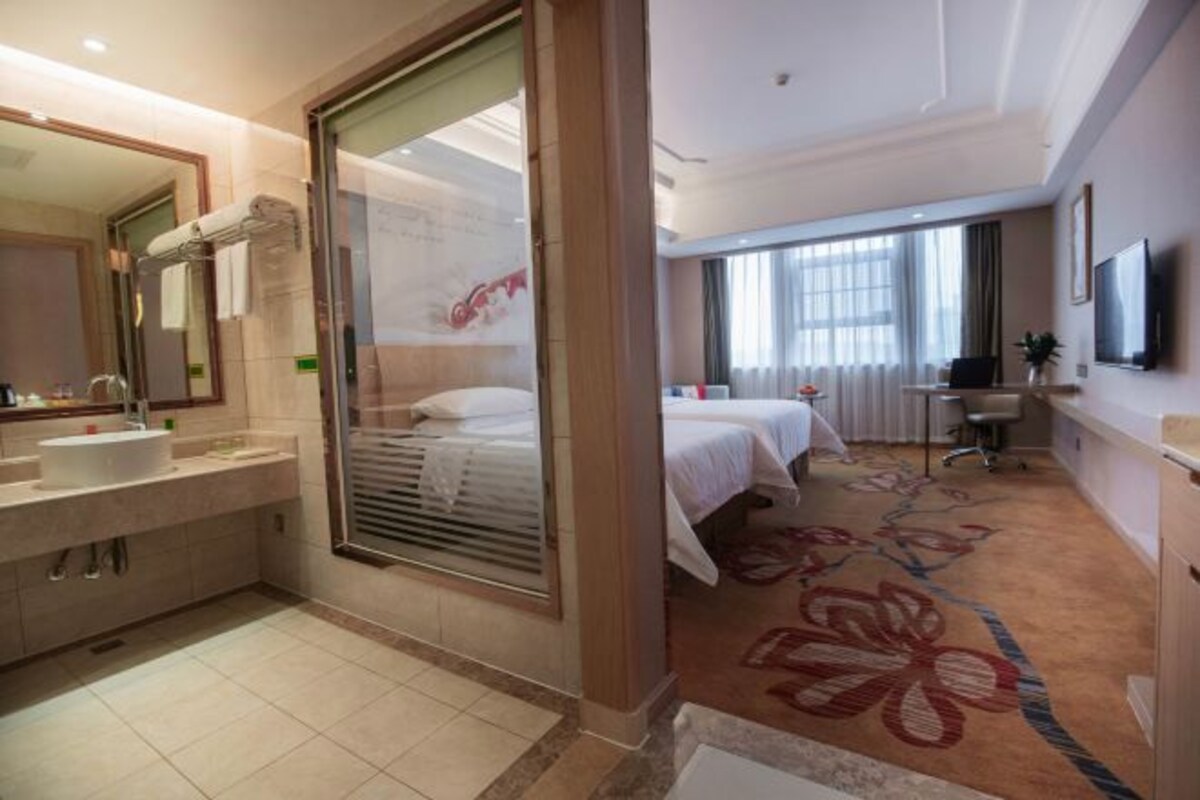A hotel room with a bathroom, a bed, a desk, and a TV.