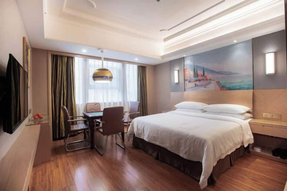 A hotel room with a bed, a desk with a chair, a television, and a painting on the wall.