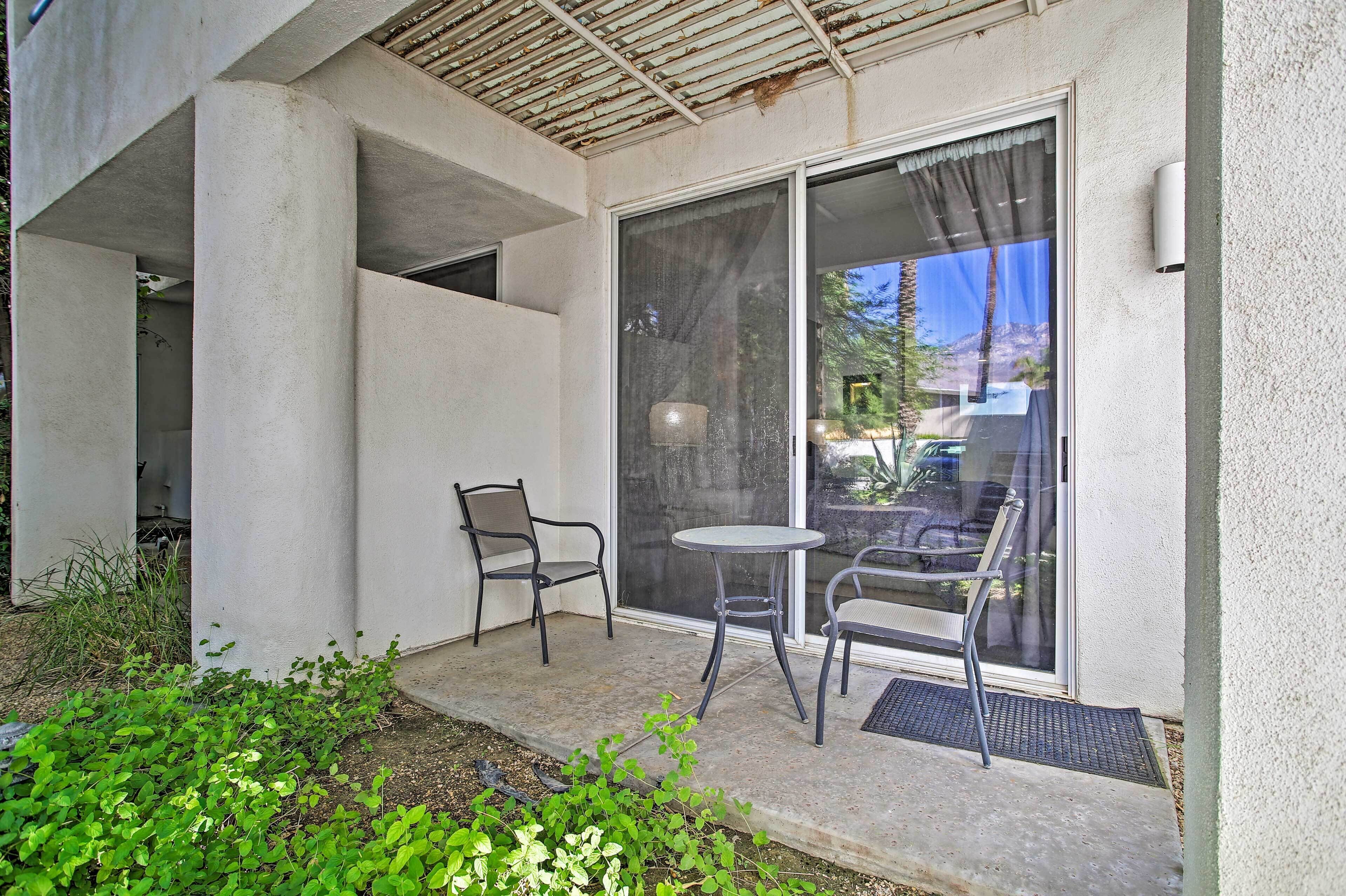 A small patio area with a table and two chairs, a sliding glass door, and a concrete structure.