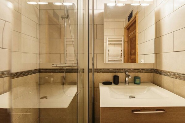 A modern bathroom with a glass-enclosed shower, a sink with a mirror, and a wooden vanity.
