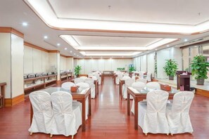 A spacious conference room with round tables and chairs, a long table with a speaker, and potted plants. - Wenhe Hotel (Hepu)
