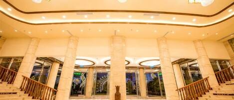 A spacious lobby with marble flooring, a central statue, and a staircase leading to upper levels.