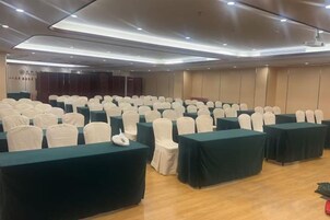 A conference room with rows of tables and chairs, a stage, and a wooden floor.