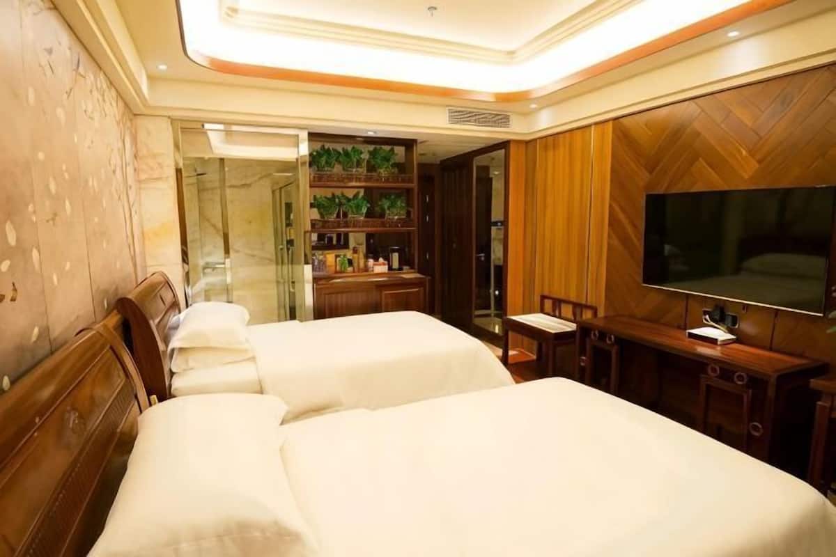 A hotel room with two beds, a TV, a desk, and a bathroom with a mirror.