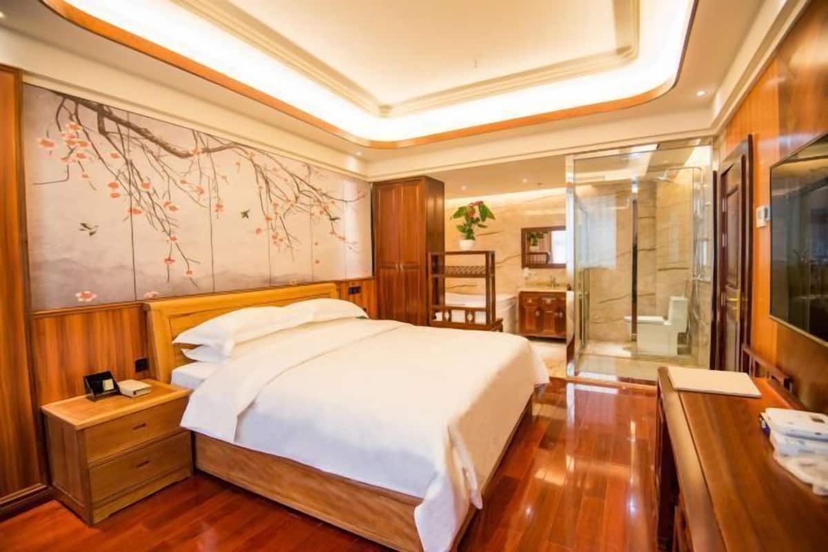 A modern hotel room with a wooden bed, a nightstand, a desk, and a large mirror.