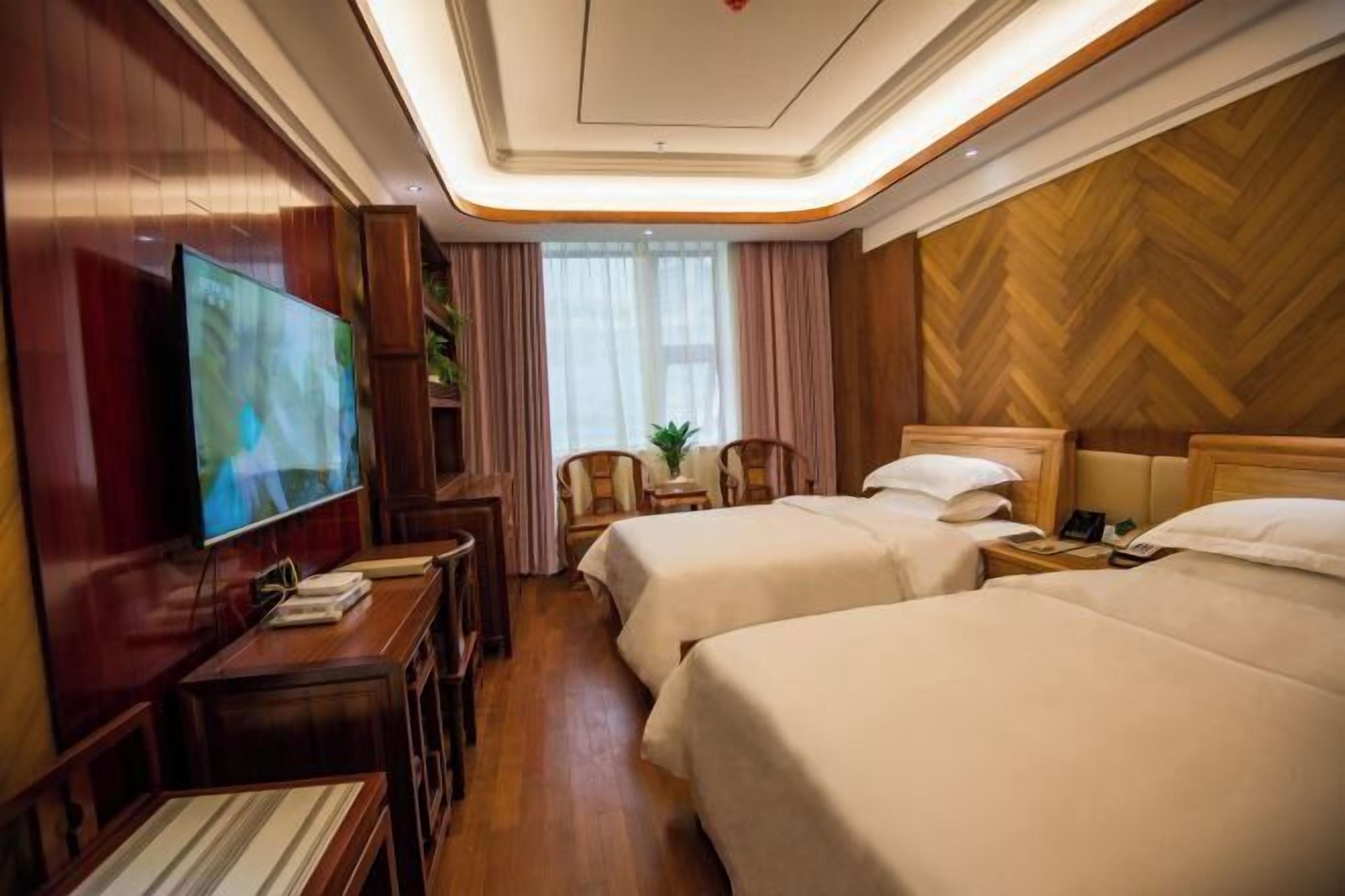 A hotel room with two beds, a TV, a desk, and a wooden wall.