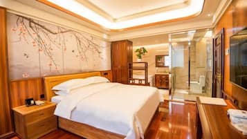 A hotel room with a wooden bed, a nightstand, a large wall painting, a bathroom with a glass shower, and a TV on a wooden table.