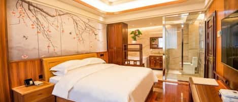 A hotel room with a wooden bed, a nightstand, a large wall painting, a bathroom with a glass shower, and a TV on a wooden table.