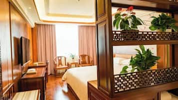 A hotel room with a bed, bedside tables, a TV, and a decorative wooden partition with plants.