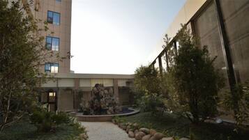 A courtyard with a central rock feature, surrounded by gravel and plants, with a building in the background.