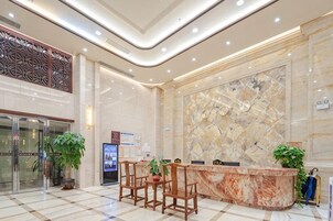 Zona de recepción de un hotel con un mostrador de mármol, sillas de madera y plantas en macetas.