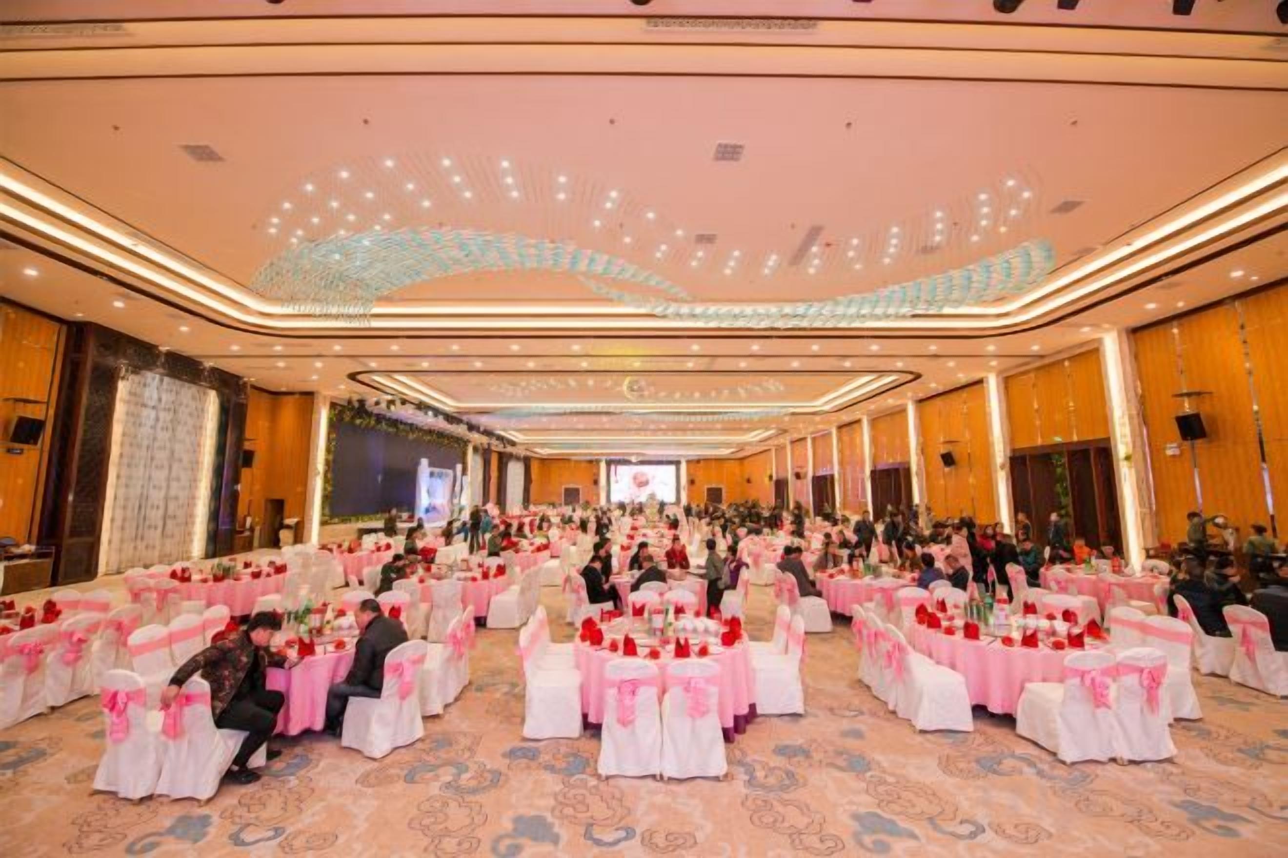 Un amplio salón de banquetes con filas de mesas, sillas y un escenario al frente.