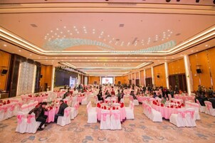 Un amplio salón de banquetes con filas de mesas, sillas y un escenario al frente.