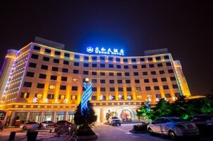 Un hotel con un letrero llamativo, varios pisos y un estacionamiento lleno de coches.